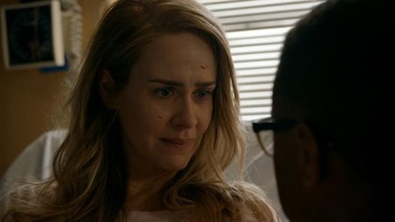 Sarah Paulson with minor blood on face sitting in hospital bed looking toward obscured face of Cuba Gooding Jr in AHS Roanoke