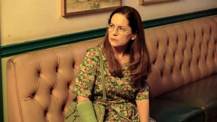 Martha Kelly as Martha sitting down on booth bench wearing green cast in FX's Baskets