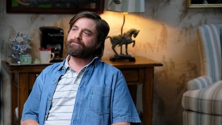 Zach Galifianakis smiling into distance in hotel room with striped armchair and horse lamp in FX's Baskets
