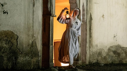 Gemma Arterton as Sister Clodagh holding lantern up by face and standing in castle doorway in FX's Black Narcissus
