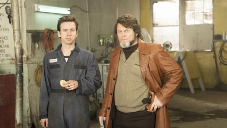 Nick Offerman as Karl in brown leather trench coat holding hand to gun on waist with man in jumpsuit in FX's Fargo Year Two