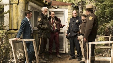 Patrick Wilson as Lou standing with other police officers with man in blue suit on wooden house porch in FX's Fargo Year Two