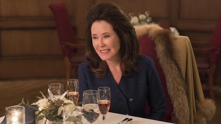 Woman with big brown hair in blue blazer dress sitting at table with champagne glasses in FX's Fargo Year Three