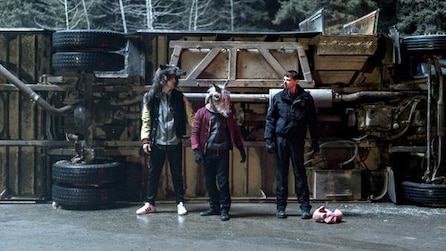 Three people wearing animal masks, hat, and mask on floor walking in front of overturned truck in FX's Fargo Year Three