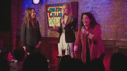 Three comedian women on stage talking to crowd at the Comedy Cellar with pink and purple stage lights in FX's Hysterical