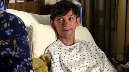 DJ Qualls as Billy in hospital gown with nose tube looking up at person in floral patterned top in FX's Legit