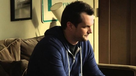 Jim Jefferies sitting on couch in blue hoodie looking down in FX's Legit