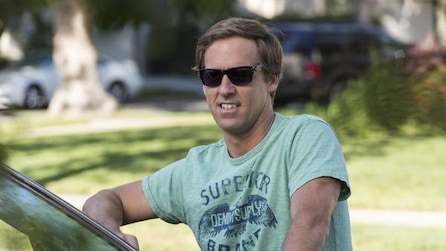 Man wearing a green shirt and leaning on a car