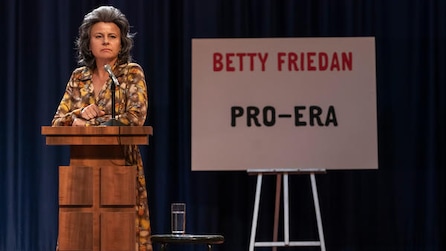 Woman standing at a podium with a microphone and a sign saying "Betty Friedan Pro-Era" behind her