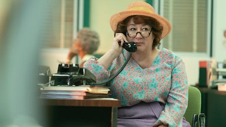 Woman wearing an orange sun hat while on the phone at a desk