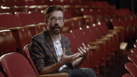 Man sitting in a theater chair talking with his hands