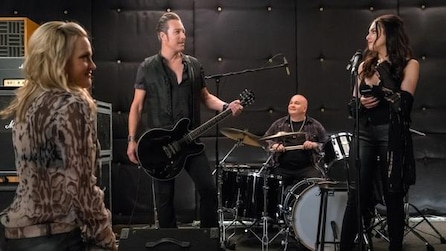 Band standing together, one person on drums, one playing the guitar and another singing