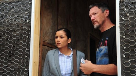 Emily Rios as Adriana Mendez standing in doorway of house wall insulation with man in black shirt in FX's The Bridge