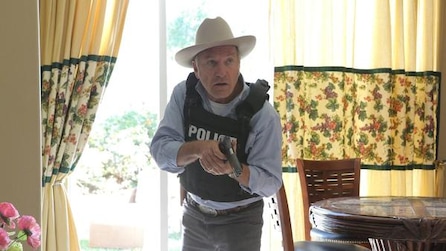 Ted Levine as Lt. Hank Wade wearing white cowboy hat and police black vest and holding gun inside house in FX's The Bridge