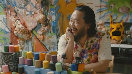 David Choe laughing with hand on face in artist studio with blocks of color and paintings on walls in FX's The Choe Show