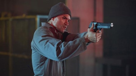 Man wearing a beanie and holding up a gun pointing at someone