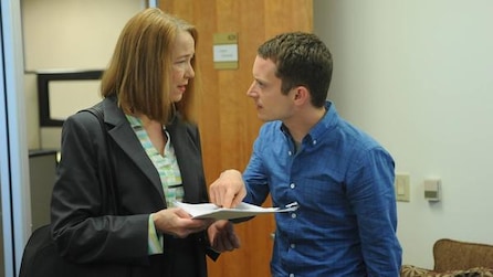 Man in a blue button down shirt talking to a woman while pointing at a piece of paper