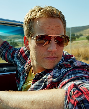 Chris Geere headshot wearing a red and blue plaid shirt and aviator sunglasses