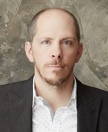 Stephen Falk Headshot wearing a white polka dot shirt with a black blazer