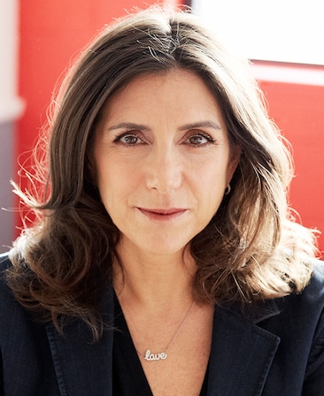 Stacey Sher headshot wearing a necklace that read "love" and a black jacket