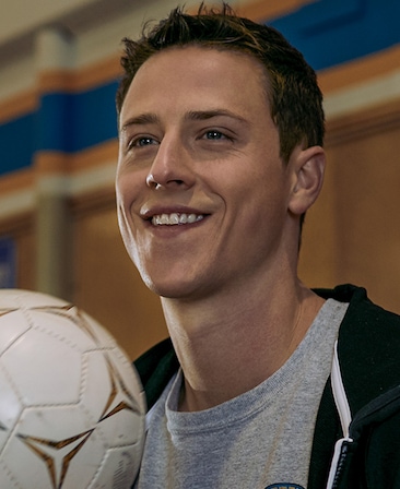 Shane Harper Headshot smiling wearing a gray shirt and holding a soccer ball
