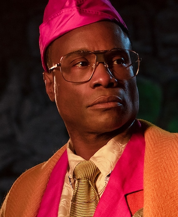 Billy Porter headshot wearing a pink hat and shirt with a tie and orange jacket