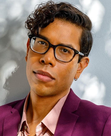 Steven Canals headshot wearing a pink shirt and jacket with black glasses
