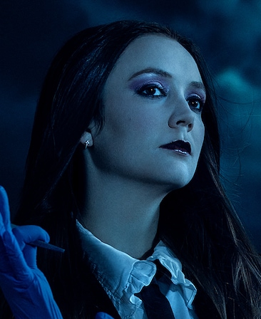 Headshot of Billie Lourd in black jacket and tie with blue glove under moonlight from FX's AHS Double Feature