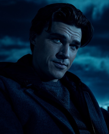Headshot of Finn Wittrock in black coat under moonlight on cloudy night from FX's AHS Double Feature