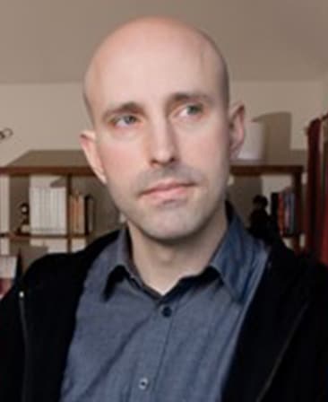 Brian K. Vaughan headshot wearing a gray button up and black jacket