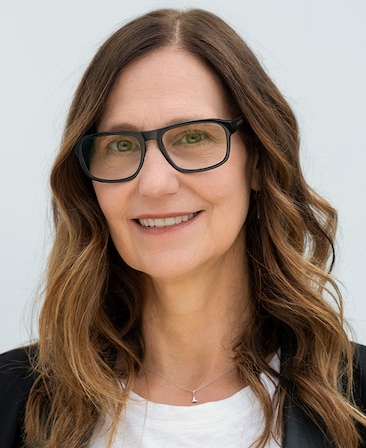 Mari Jo Winkler-Ioffreda headshot wearing a white shirt, black jacket and black glasses