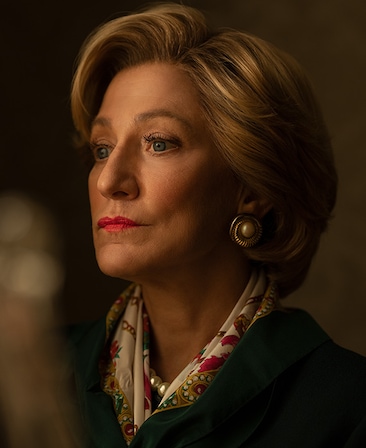 Headshot of Edie Falco as Hillary Clinton wearing green coat and white patterned scarf from FX's American Crime Story