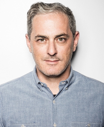 John Lesher headshot wearing a gray shirt with white buttons