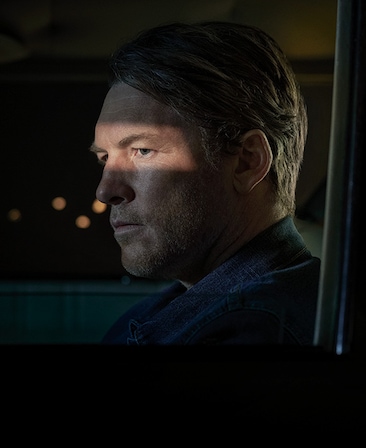 Sam Worthington headshot by a window at night in the dark
