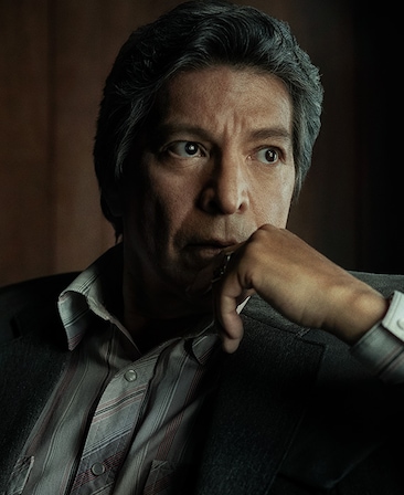 Gil Birmingham headshot wearing a striped shirt and placing his hand on his chin