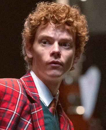 Thomas Brodie-Sangster headshot wearing a red plaid jacket and green top