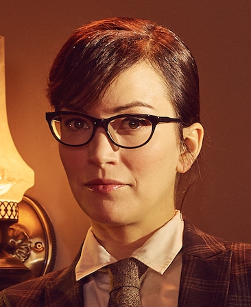 Britt Lower headshot wearing black glasses with a white shirt, tie and plaid jacket