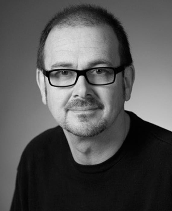 Black and white headshot of Chris Long wearing glasses in black shirt against grey gradient background