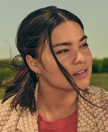 Devery Jacobs headshot outside wearing an orange shirt layered with a flower patterned top over.