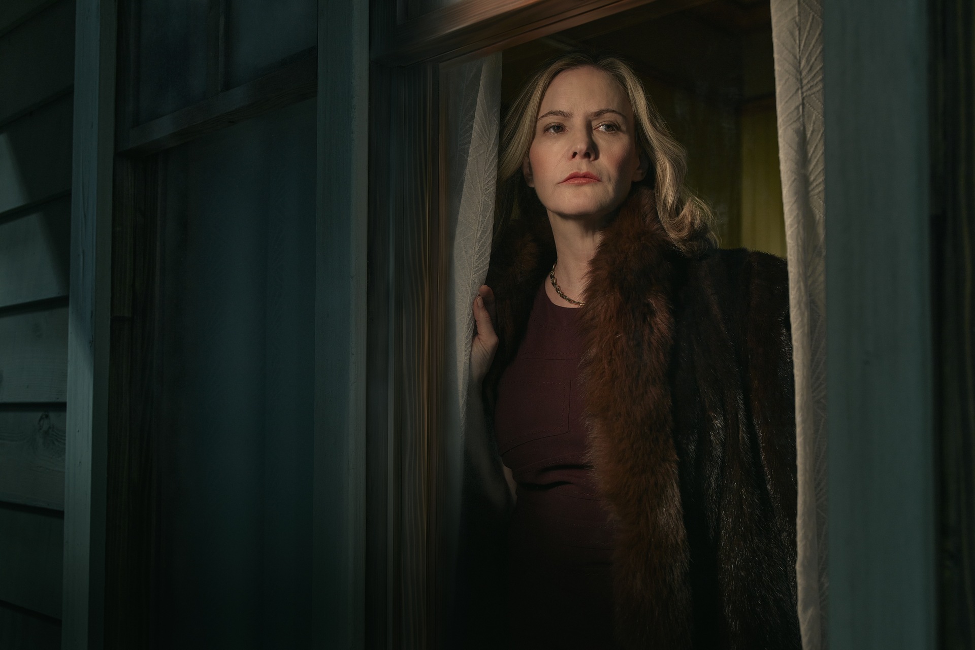 Woman with blonde hair looking through curtain windows. 