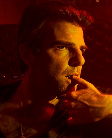 Headshot of Zachary Quinto looking off to the side with thumb on lips and red lighting on face