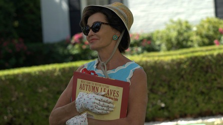 Jessica Lange as Joan Crawford wearing blue and white dress holding Autumn Leaves record outside in Feud FX show