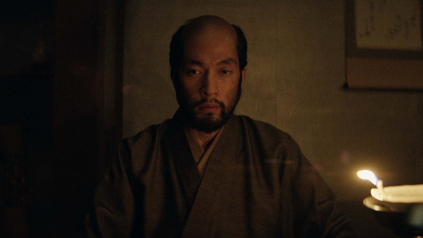 Close up of Buntaro sitting in Blackthorne's house lit by fire light