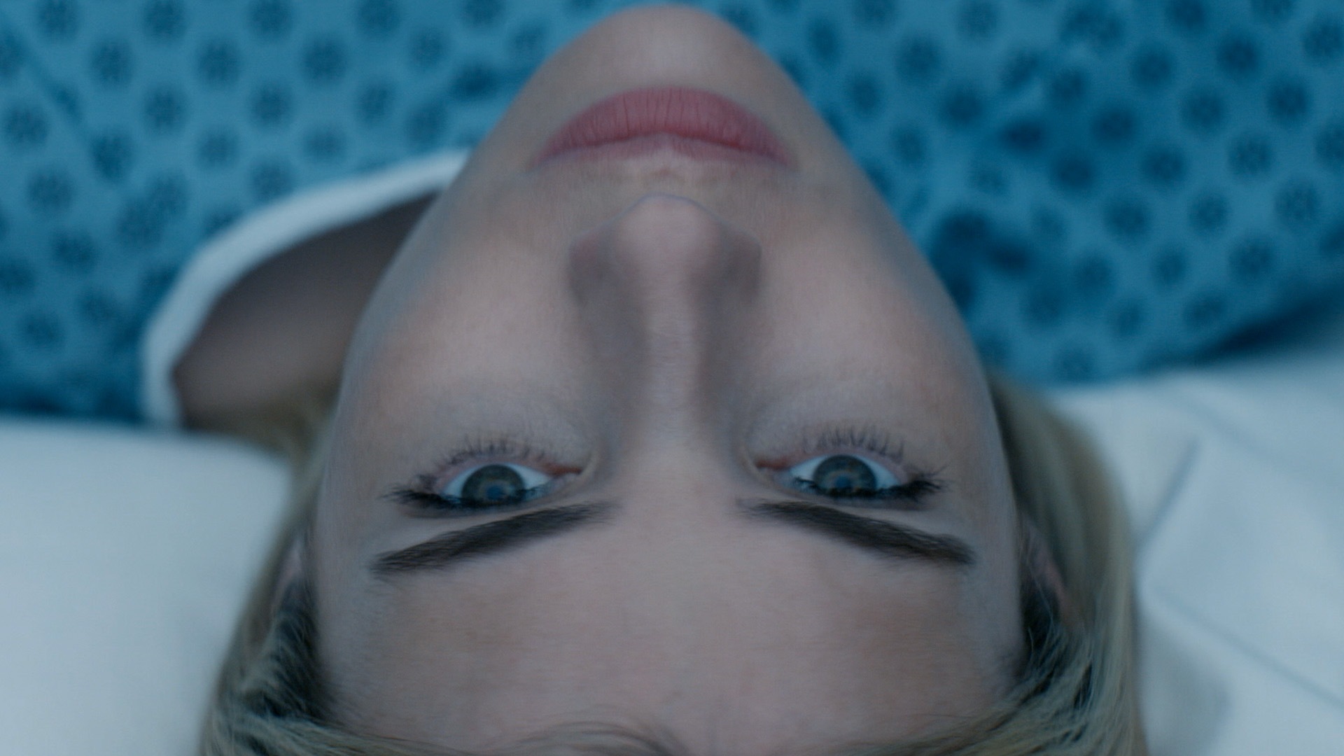 A woman laying down on a white bed wearing a hospital gown.