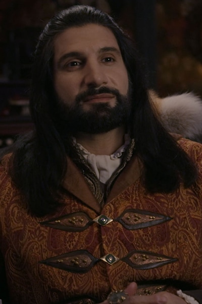 Nandor with long black hair with a smirk on his face
