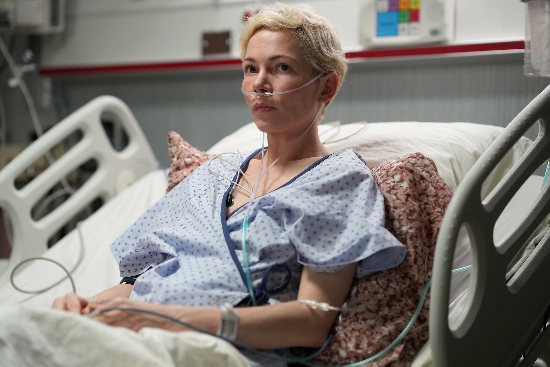 Molly sitting in a hospital bed wearing a blue hospital gown and breathing tubes in her nose in FX's Dying for Sex
