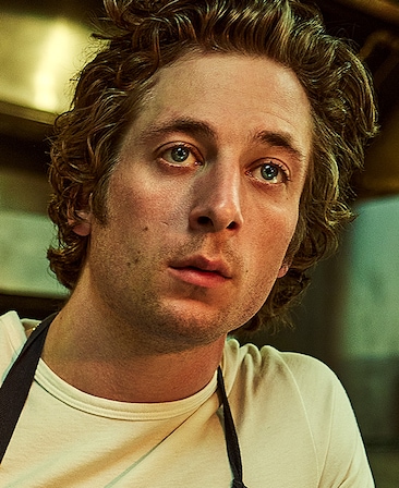 Jeremy Allen White headshot in white shirt and blue apron