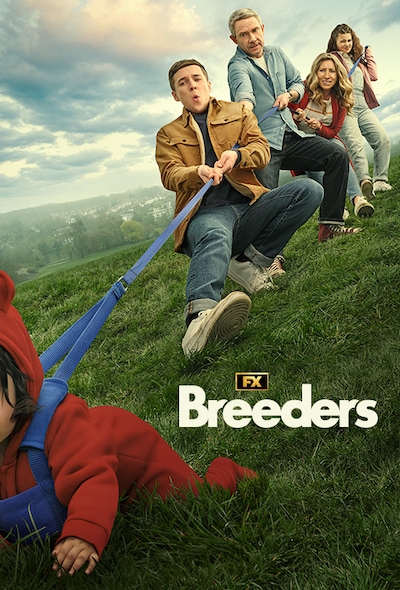 Cast of Breeders family amid a grassy field pulling on a rope tethered to a crawling baby dressed in a red onesie