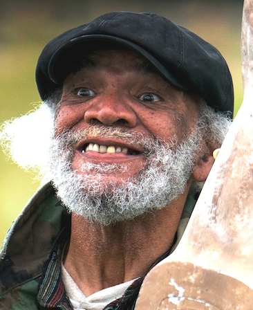 Paul Barber headshot wearing a black hat and camo print jacket, standing outside.