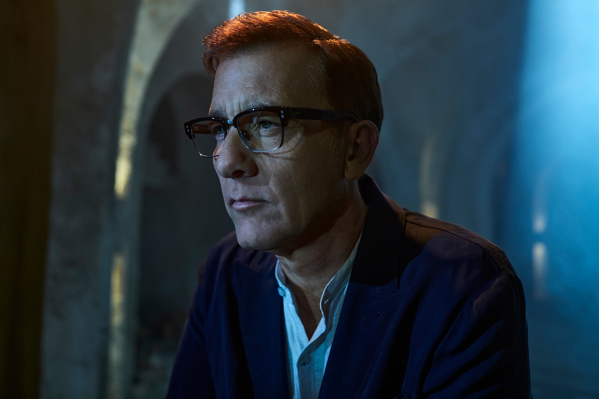 Clive Owen as Andy Ronson wearing glasses and a navy sweater 